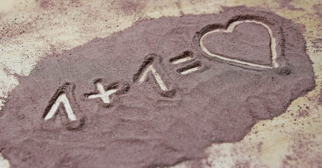 Equation written in sand with 1+1 equals heart. Expresses love and creativity.